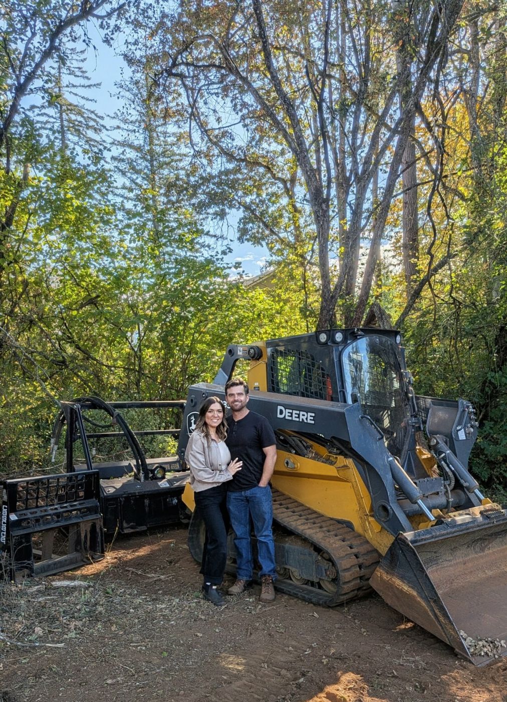 Nathan and Tina standing in front of the John Deere track loader on a job site